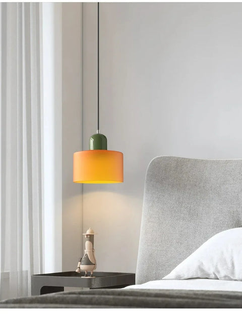 Amber glass pendant light with an olive cap beside a bed