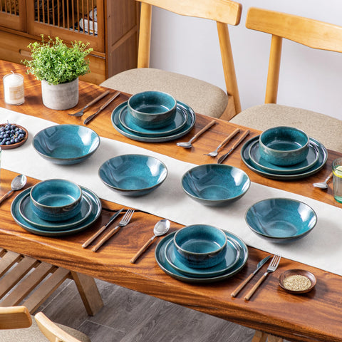 Teal reactive glaze plates and bowls laid along a wooden dining table