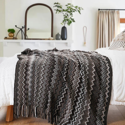 Black boho tasselled throw across the end of a bed