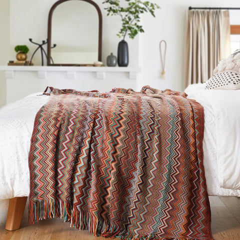 Dusty red boho tasselled throw across the end of a bed