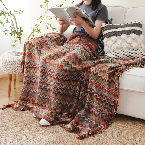 Woman reading on a sofa under a dusty red boho tasselled throw