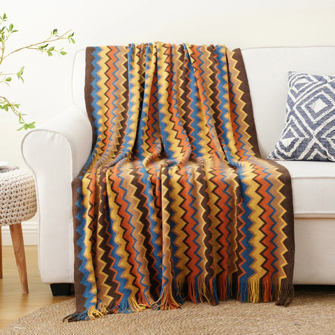 Orange boho tasselled throw draped over a white sofa
