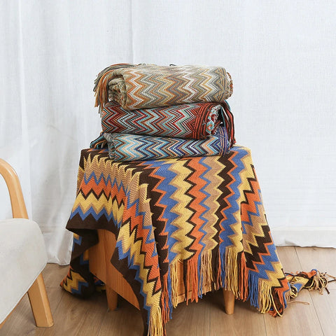 Boho tasselled throws folded in a stack on a stool, in several colourways