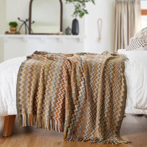 Mustard boho tasselled throw across the end of a bed