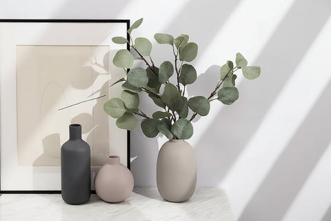 Ceramic table vases with foliage against a white wall