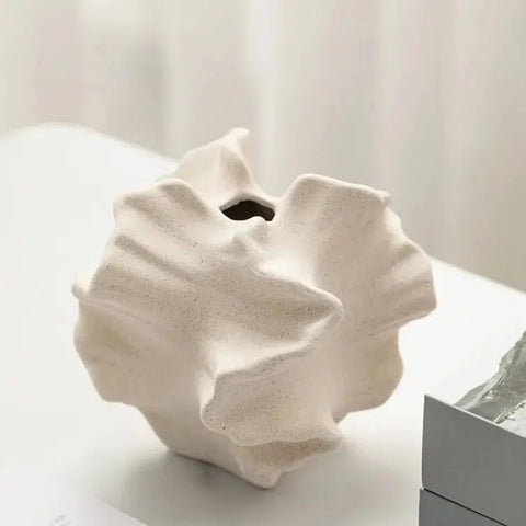 Coral ceramic vase on a white surface, showing the ruffled shell form