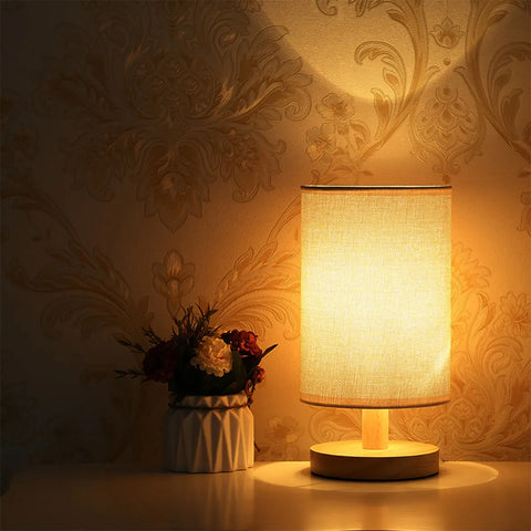 Cylinder bedside lamp lit in a dark room with dried flowers