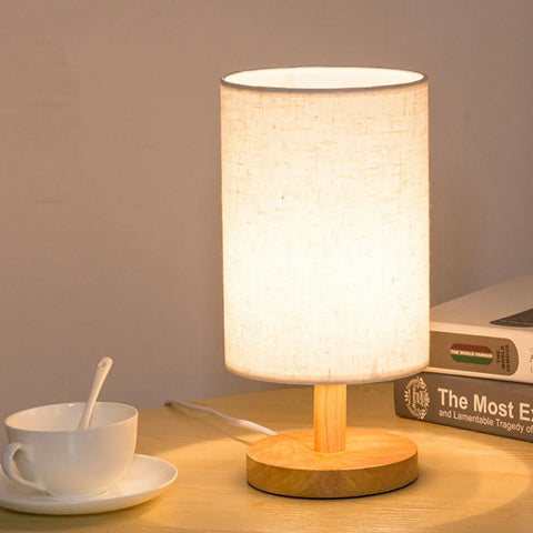 Cylinder bedside lamp lit on a desk beside a cup of coffee