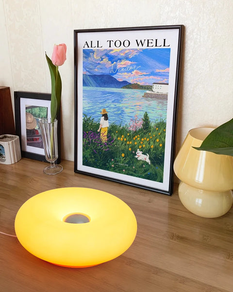 Donut table lamp lit on the floor beside framed pictures and tulips