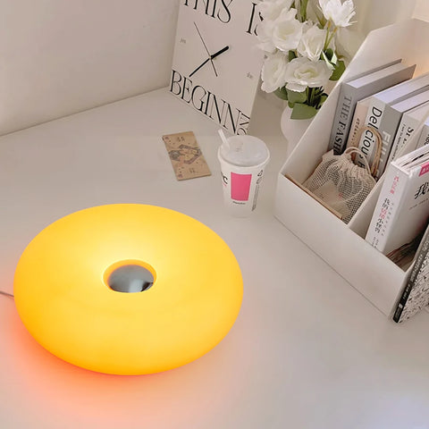 Orange donut table lamp lit on a desk beside a magazine rack