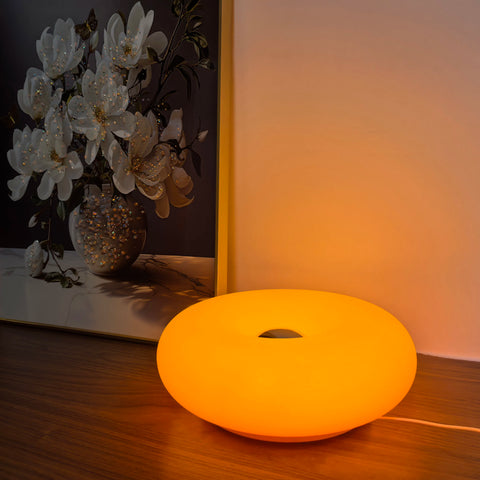 Orange donut table lamp lit on a table beside dried hydrangea