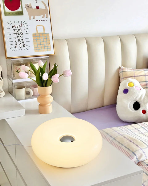 White donut table lamp lit on a bedside table with tulips