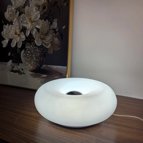 White donut table lamp on a wooden table beside a vase