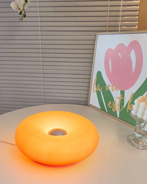 Donut table lamp lit on a desk beside a framed print