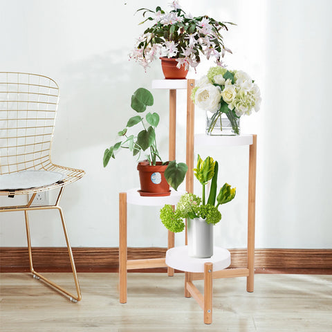 Stepped bamboo plant stand with four potted plants against a white wall