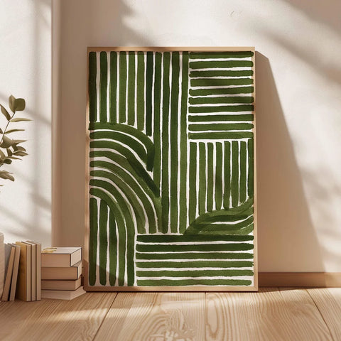 Framed abstract art with green and white lines on a wall in a room with books and a plant.