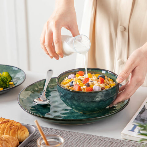 Hands holding a deep green stoneware bowl of food
