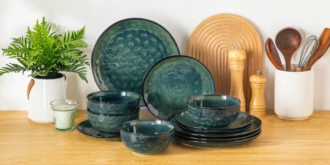 Green stoneware dinner set stacked beside wooden kitchen utensils