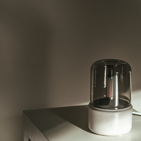 White Mistt aroma diffuser lit on a shelf against a plain wall