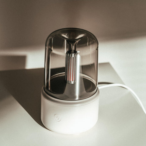 Mistt aroma diffuser in white with a clear glass chamber, on a pale surface
