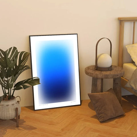 Modern gradient art print framed on a wall beside a plant and side table