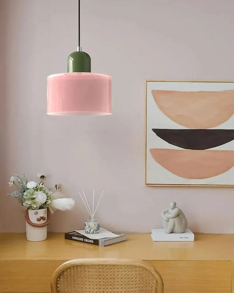 Pink glass pendant light with an olive cap above a wooden desk