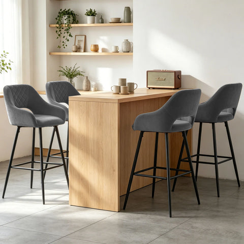 Four grey velvet quilted bar stools with arms at a wooden counter
