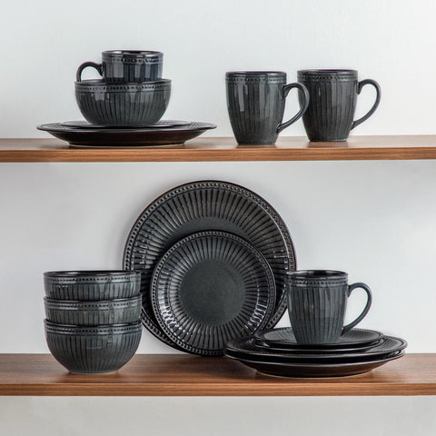 Ribbed stoneware plates, bowls and mugs stacked on a plain background