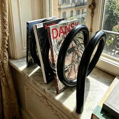 Spiral magazine rack in black, holding magazines by a window