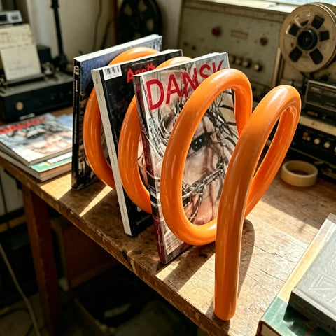 Spiral magazine rack in orange, holding magazines on a table