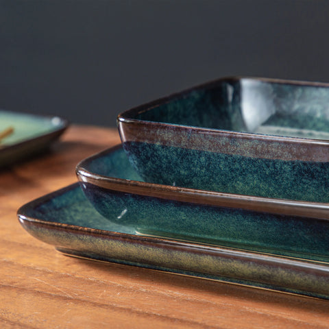 Stack of square green stoneware plates and rectangular serving dishes