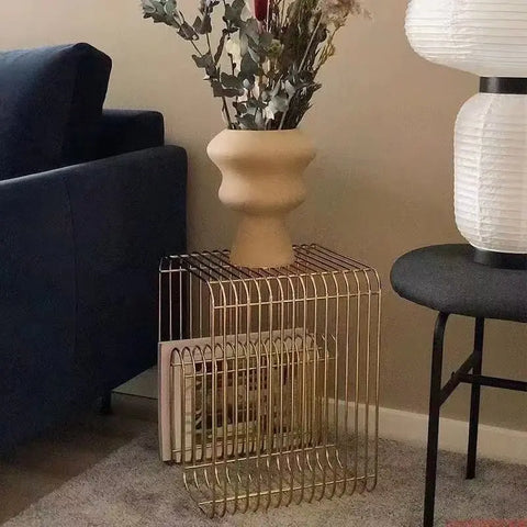 Gold wire side table beside a navy sofa with a vase on top