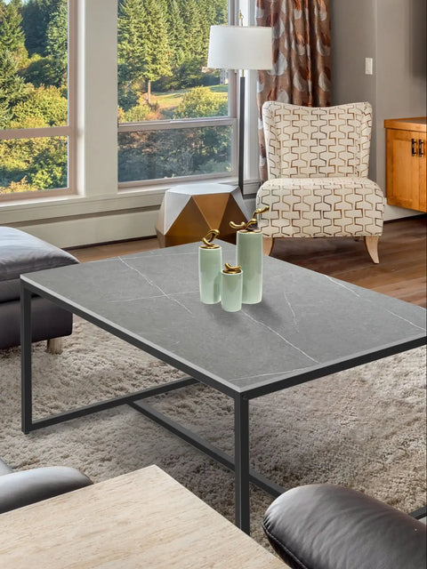 Stone and metal coffee table styled with glassware beside a window