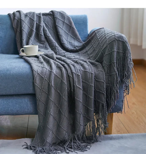 Charcoal tasselled knitted throw draped over a blue sofa