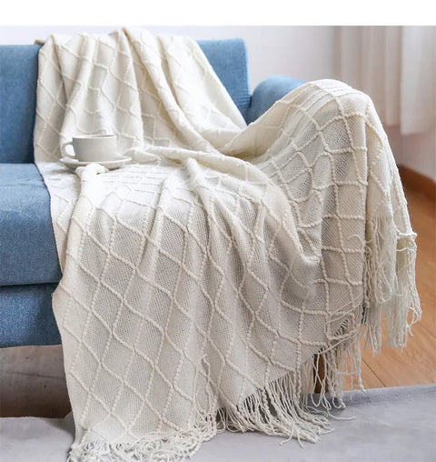 Cream tasselled knitted throw draped over a blue sofa