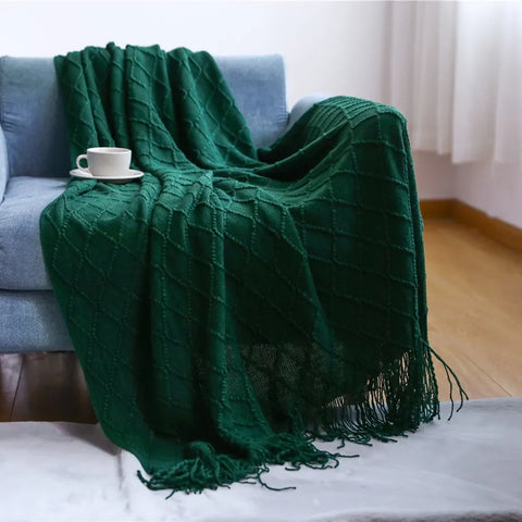 Dark green tasselled knitted throw draped over a blue sofa