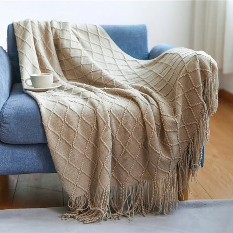 Sand tasselled knitted throw draped over a blue sofa