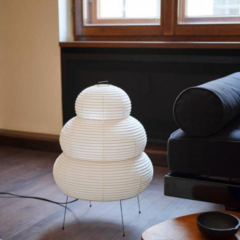 Tiered paper lantern lamp lit on a wire tripod beside a window
