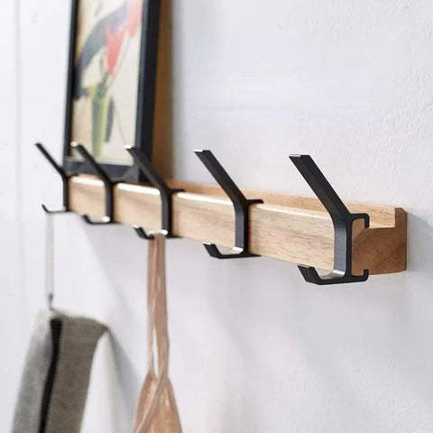 Wall-mounted coat rack in black with five folding hooks, hung with coats