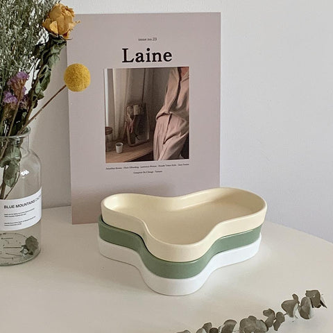 Beige and green Cloud accessory trays stacked beside a book and dried flowers