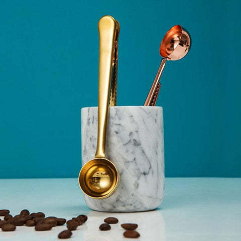 Gold coffee scoop clips in a marble pot with coffee beans