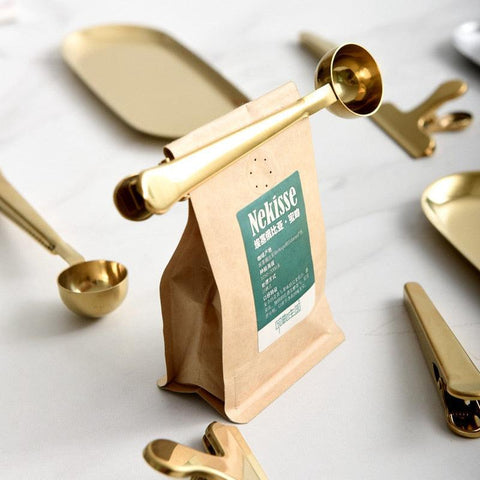 Gold coffee scoop clip beside a sealed coffee bag