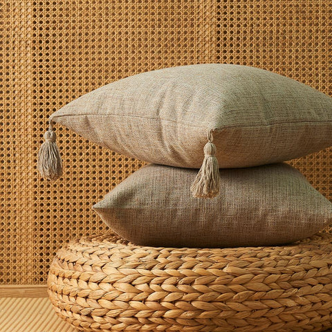 Two hemp cushion covers in beige and brown on a woven pouffe