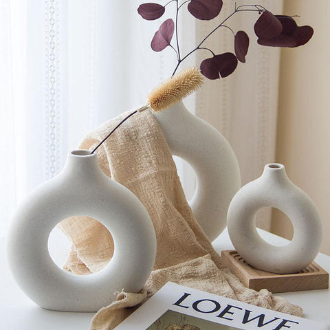 Donut vase holding dried stems against a pale wall