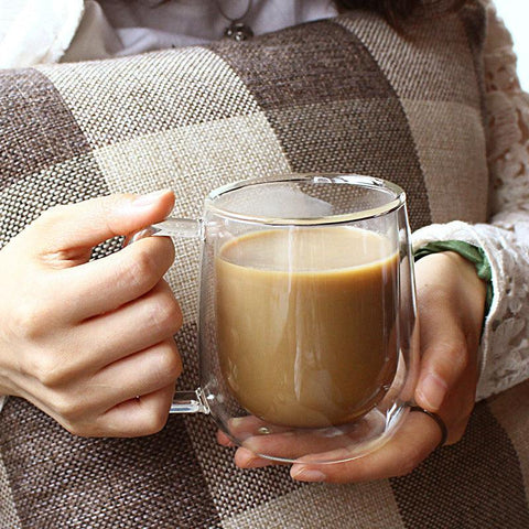 Double walled glass mug held in both hands on a sofa
