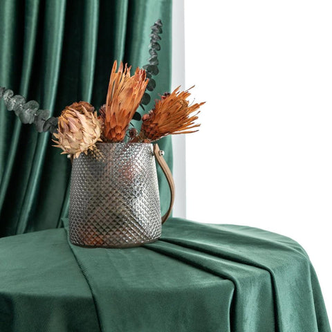 Dark green velvet curtain beside a vase of dried pampas