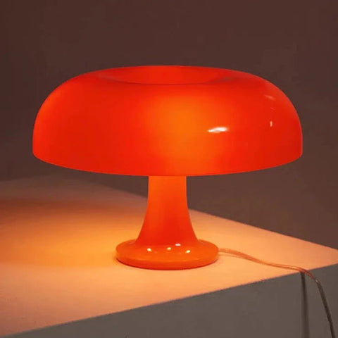 Orange mushroom table lamp lit on a table top, casting a warm glow