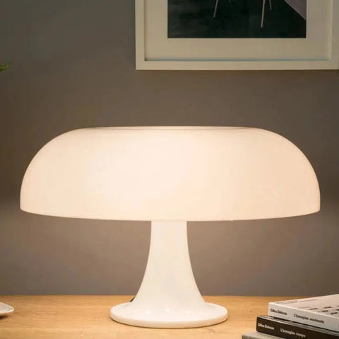 White mushroom table lamp lit on a sideboard below a framed picture