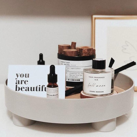 Round footed storage tray in white holding skincare bottles