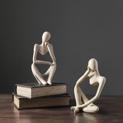 Two stone Thinker sculptures on books against a grey background